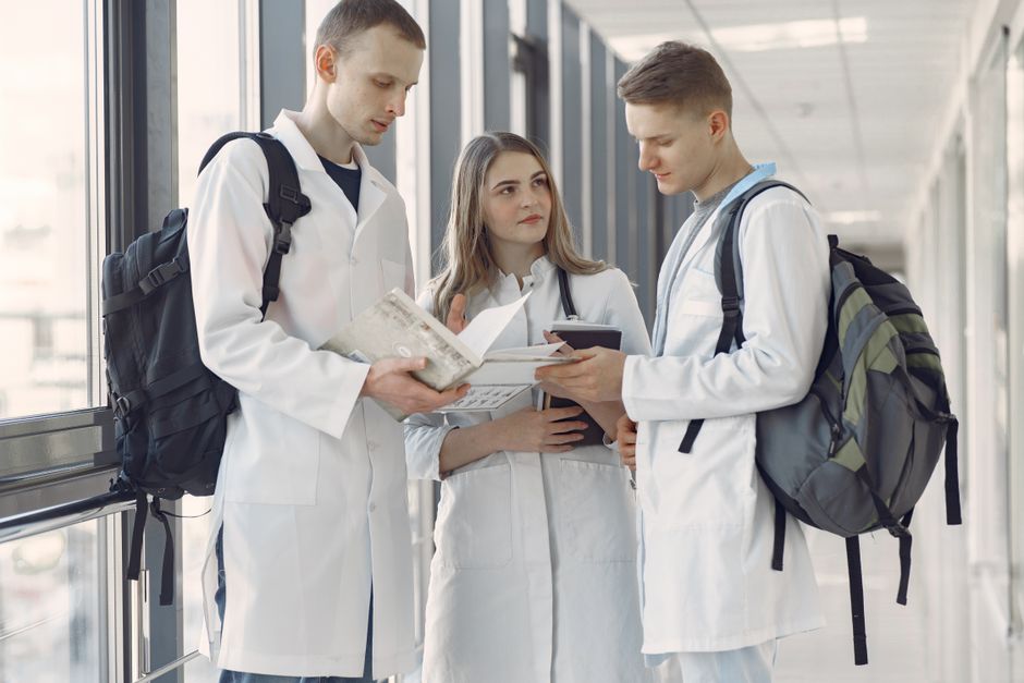Three medical students in a hospital hallway sharing notes and learning together.