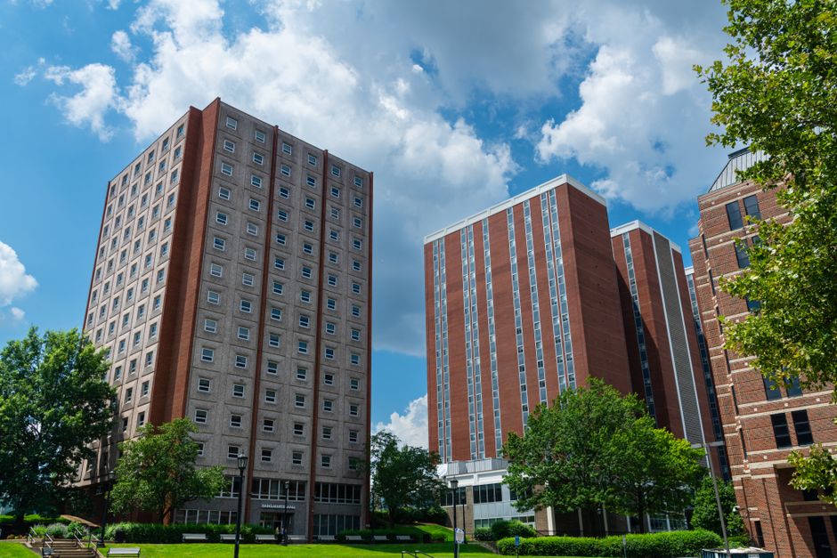 Tall brick residential buildings on a college campus under a vibrant blue sky with clouds.