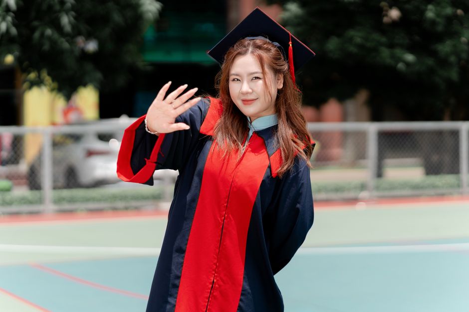 Cheerful graduate waving in traditional cap and gown on graduation day.