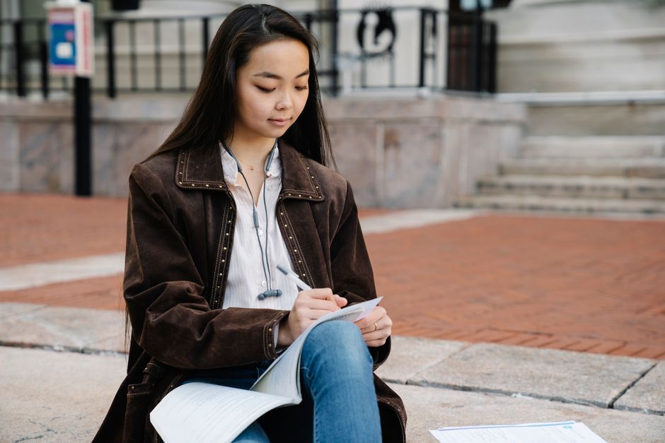 Student sitting outdoors on campus, focused on studying and writing notes.