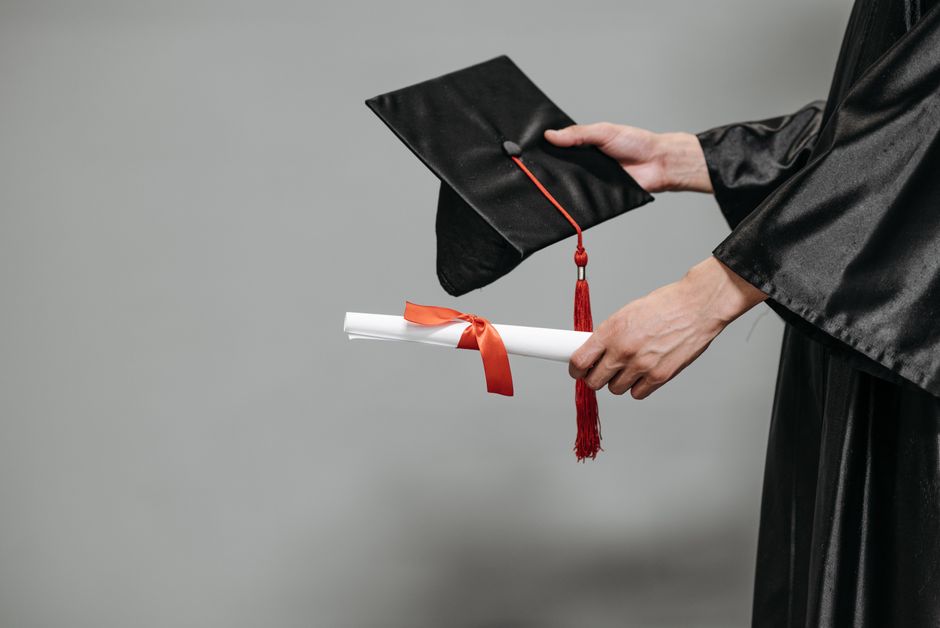 Close-up of graduate holding cap and diploma with red ribbon, symbolizing success.