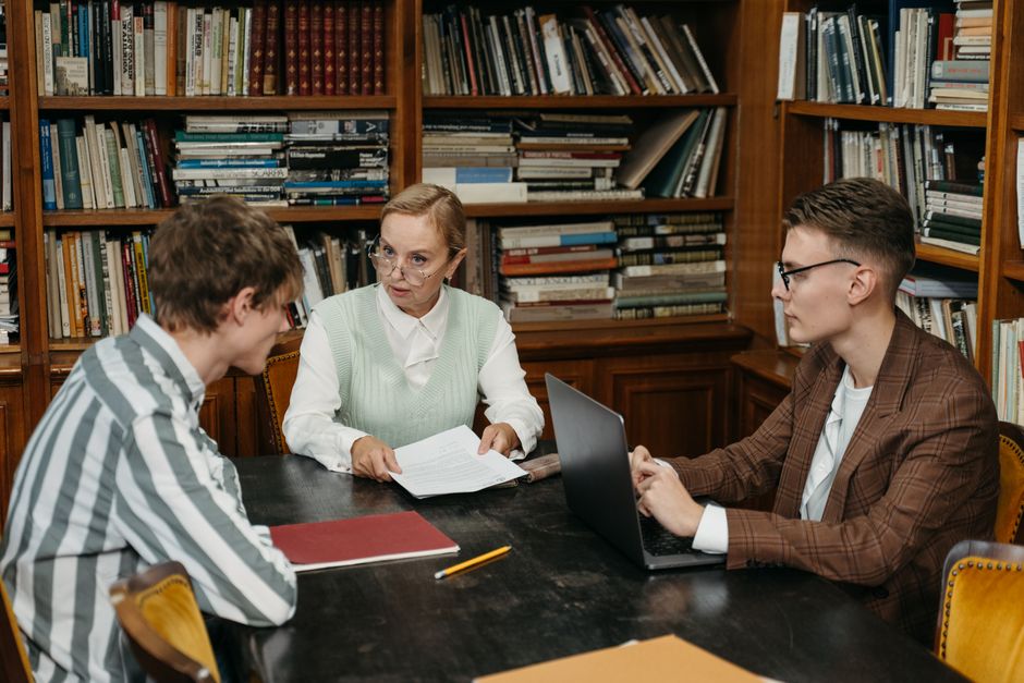 A group of adults engaged in conversation around a table in a library setting.