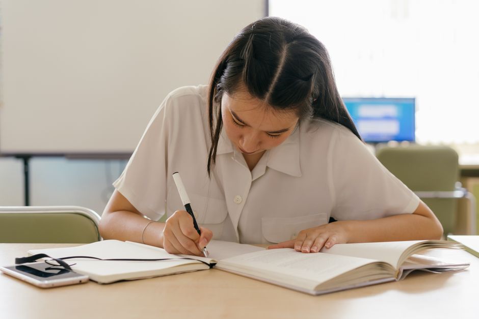 Young woman engaged in studying at a classroom desk with books.
