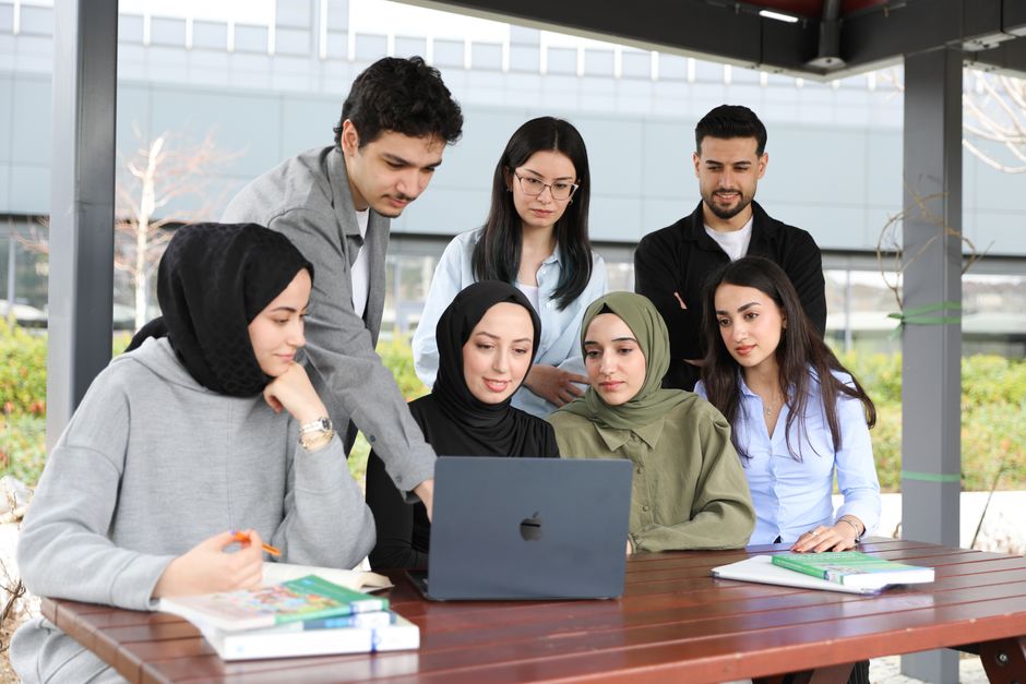 A group of young adults engage in collaborative studying outdoors, sharing ideas around a laptop.