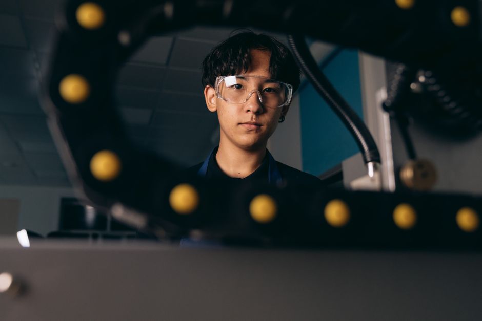 Young engineer focused on work, wearing protective goggles in a dimly lit workshop environment.