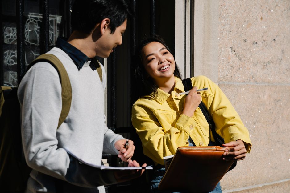 Two young students smiling and chatting outdoors at college, enjoying a sunny day.