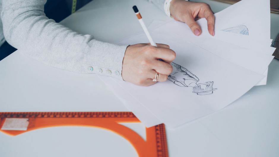 Close-up of an artist designing fashion sketches while seated at a desk indoors.