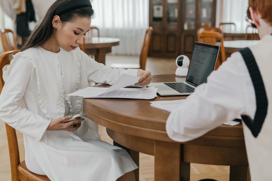 Two students focusing on their studies at a communal table, using laptops and documents.